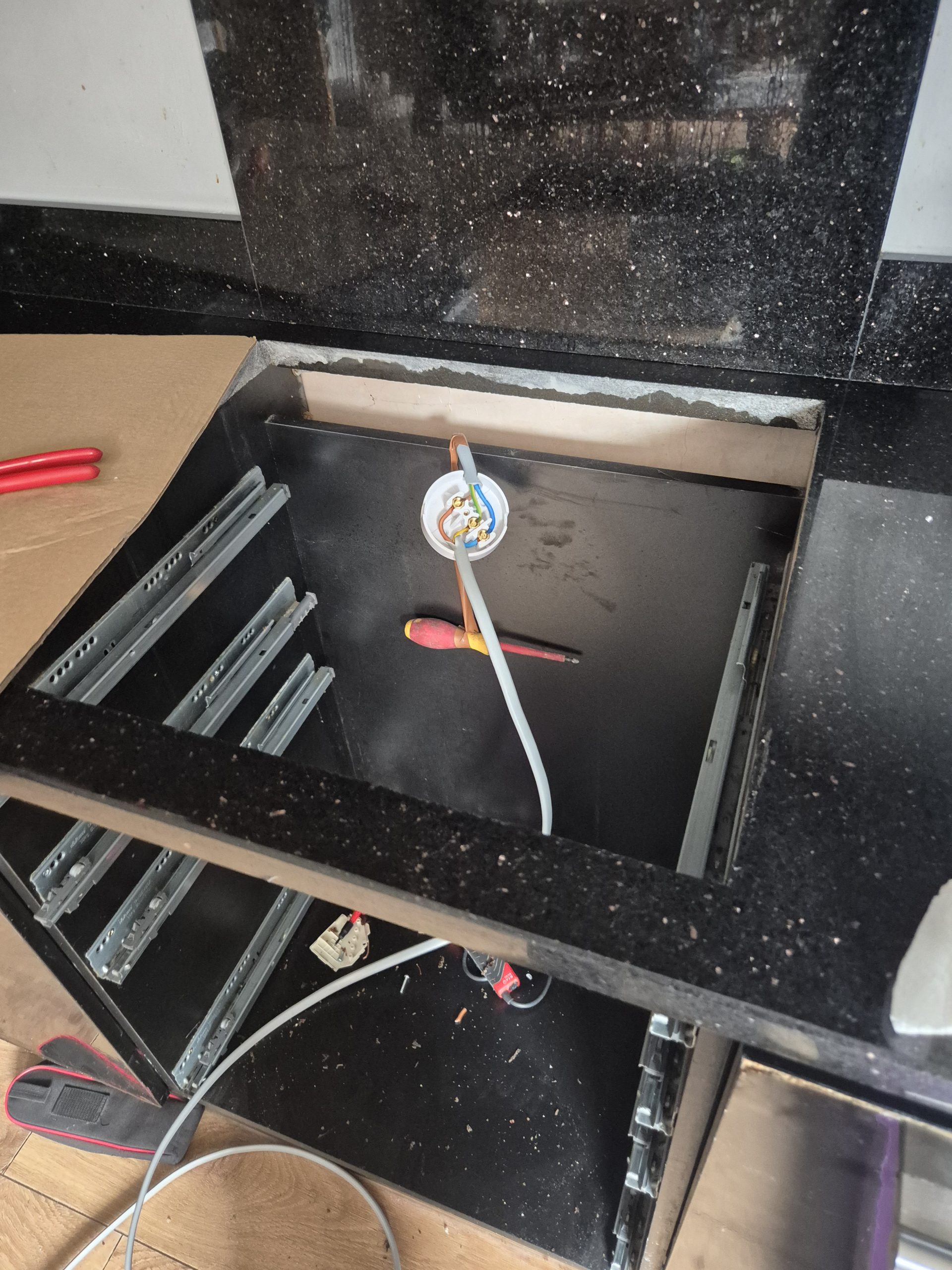 Kitchen electric cooker install with wiring exposed and screwdriver